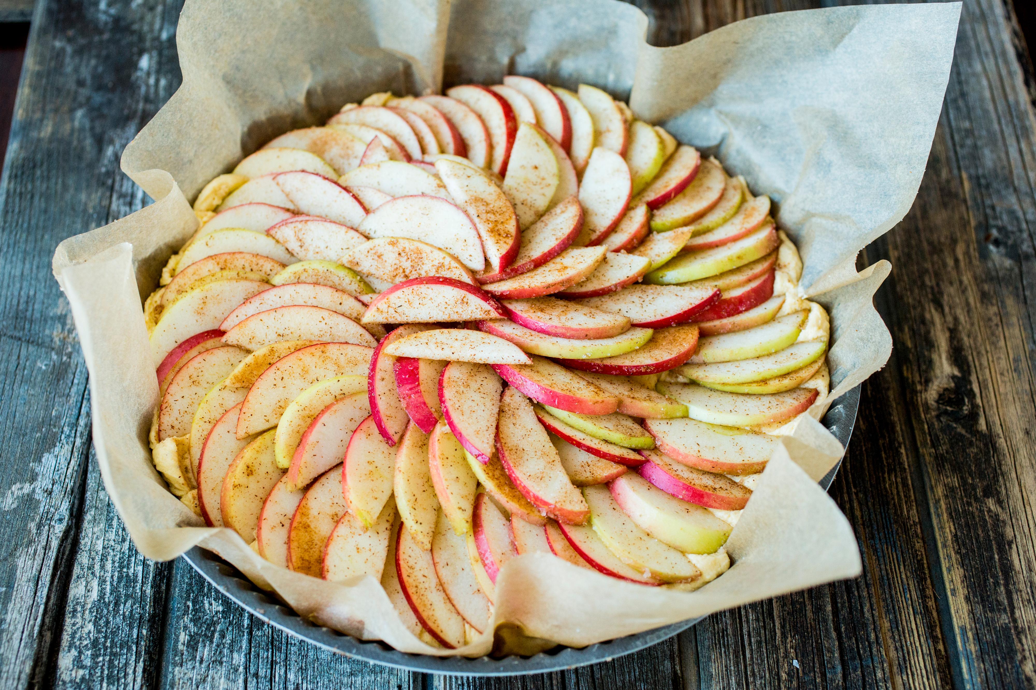 Skrell eplene og skjær dem i tynne skiver. Vend skivene sammen med sukker og kanel og fordel epleskivene jevnt utover kakerøren.