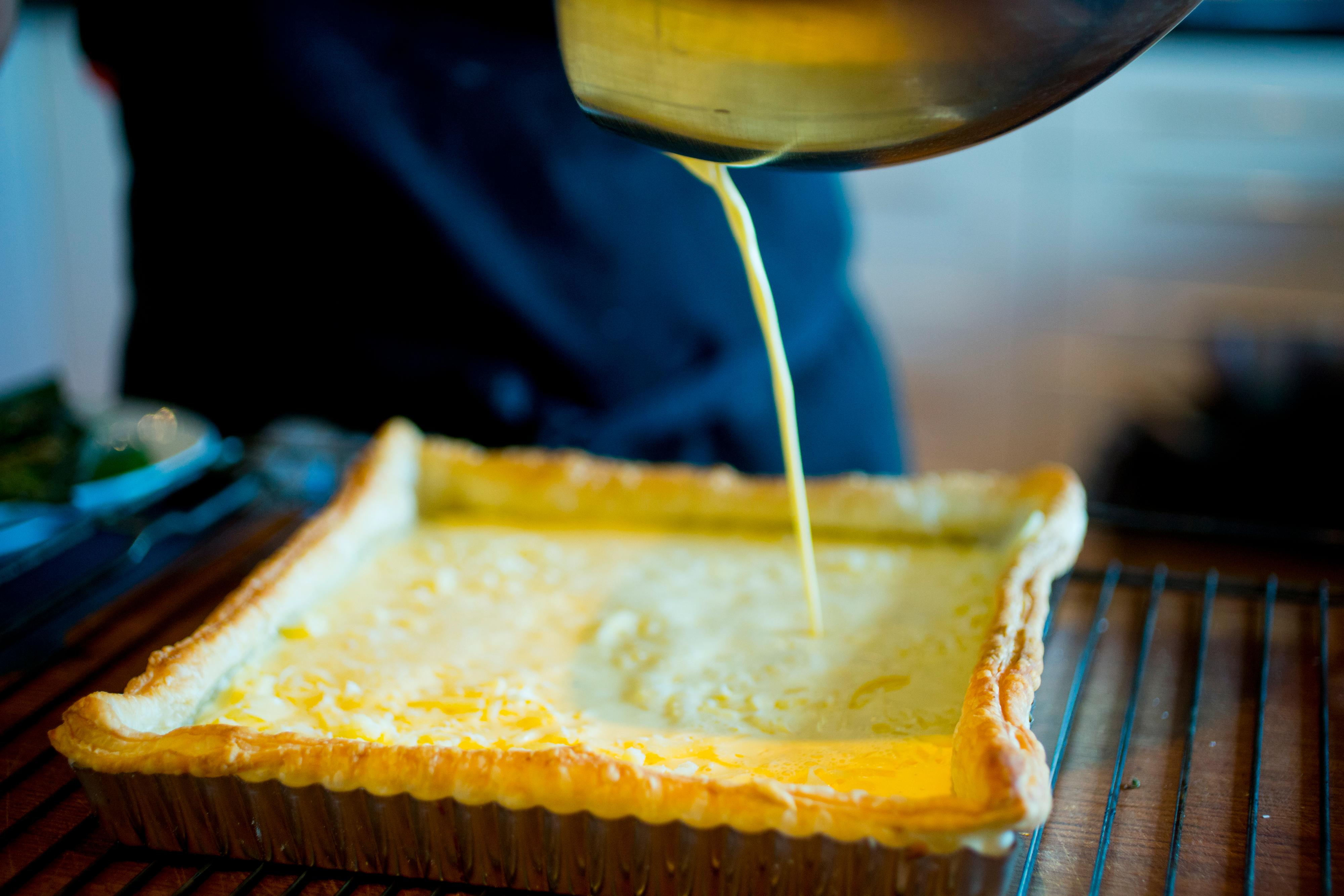 Visp sammen egg, matfløte, litt salt og kvernet pepper. Fordel den revne osten jevnt utover butterdeigsbunnen. Legg i asparges og vårløk tett i tett.