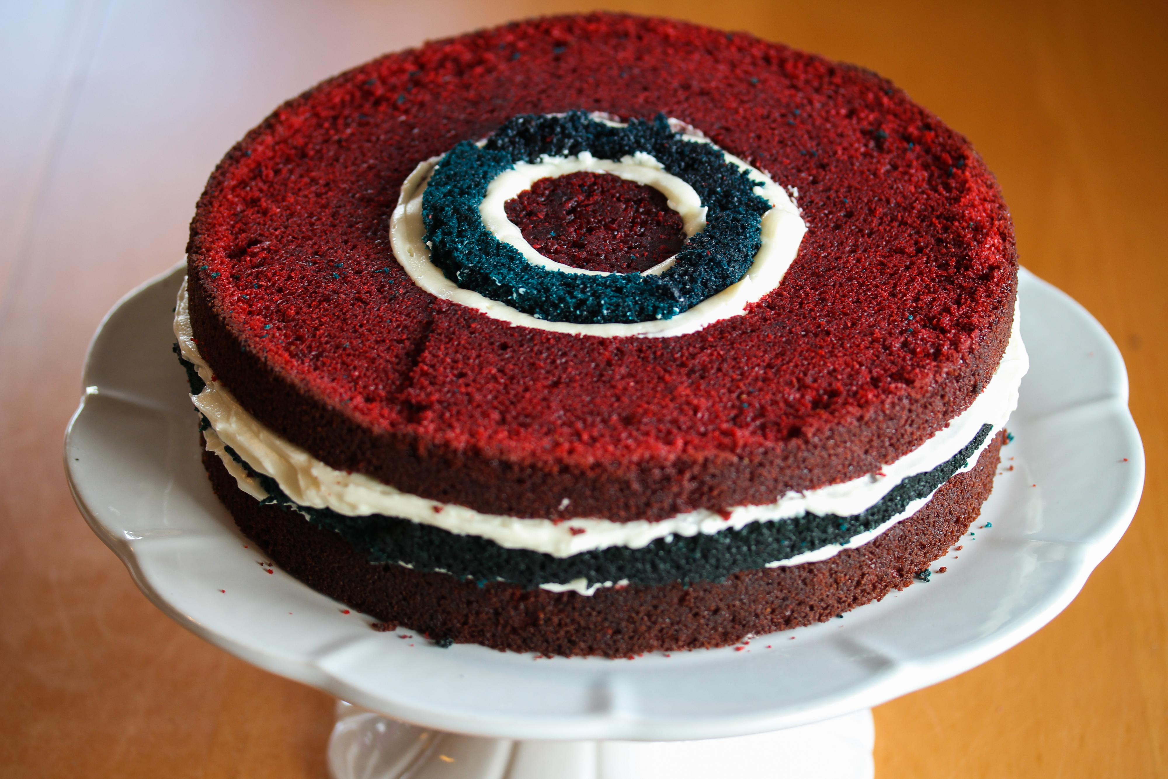 Legg på den siste røde kakeringen og den lille, røde kaken i midten. Fyll igjen opp mellomrommet mellom blå og røde kaker ved å sprøyte inn ostekrem. Hvis den blå kaken igjen er litt lavere, kan du fylle på med blå kakerester for å få samme høyde på kaken.