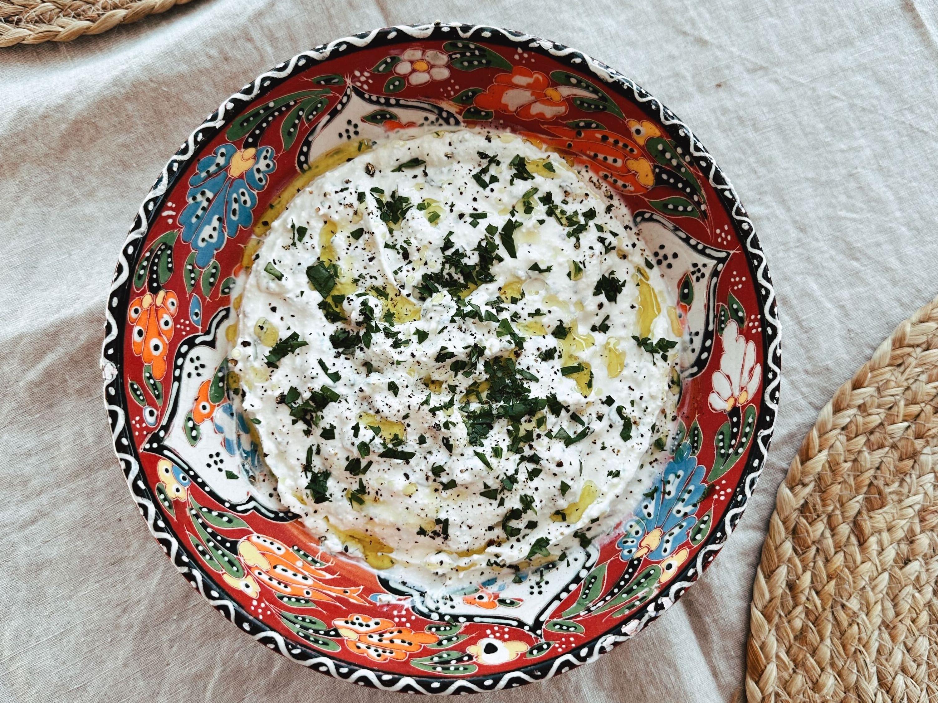Kremet fetadipp i en skål toppet med olivenolje og urter