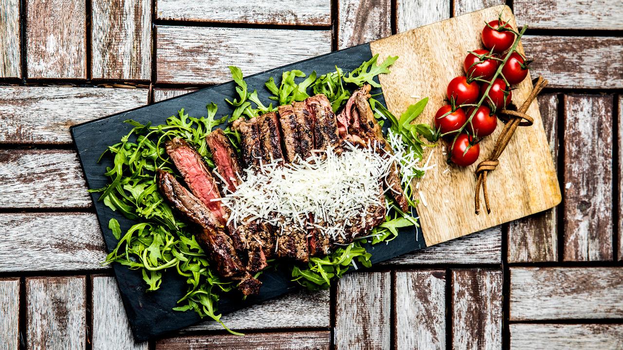 grillet entrecôte med ruccola og parmesan på sort og trefarget fjøl