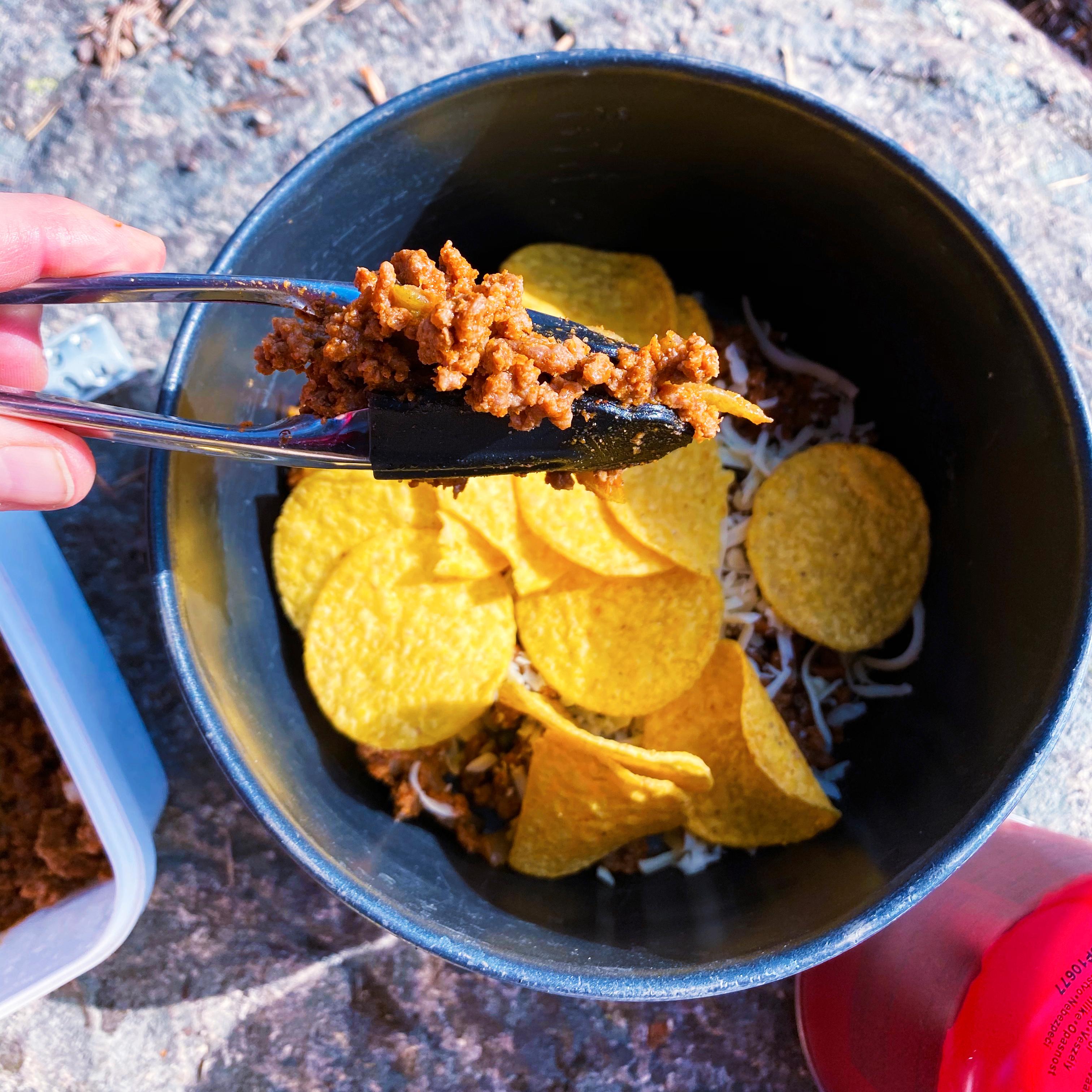 Ha litt smør i bunnen av primuskjelen. Sett blussen på lav varme slik at nachosen ikke svir seg. Legg lagvis kjøttmiks, ost og nachos. Legg også nachos langs kantene.