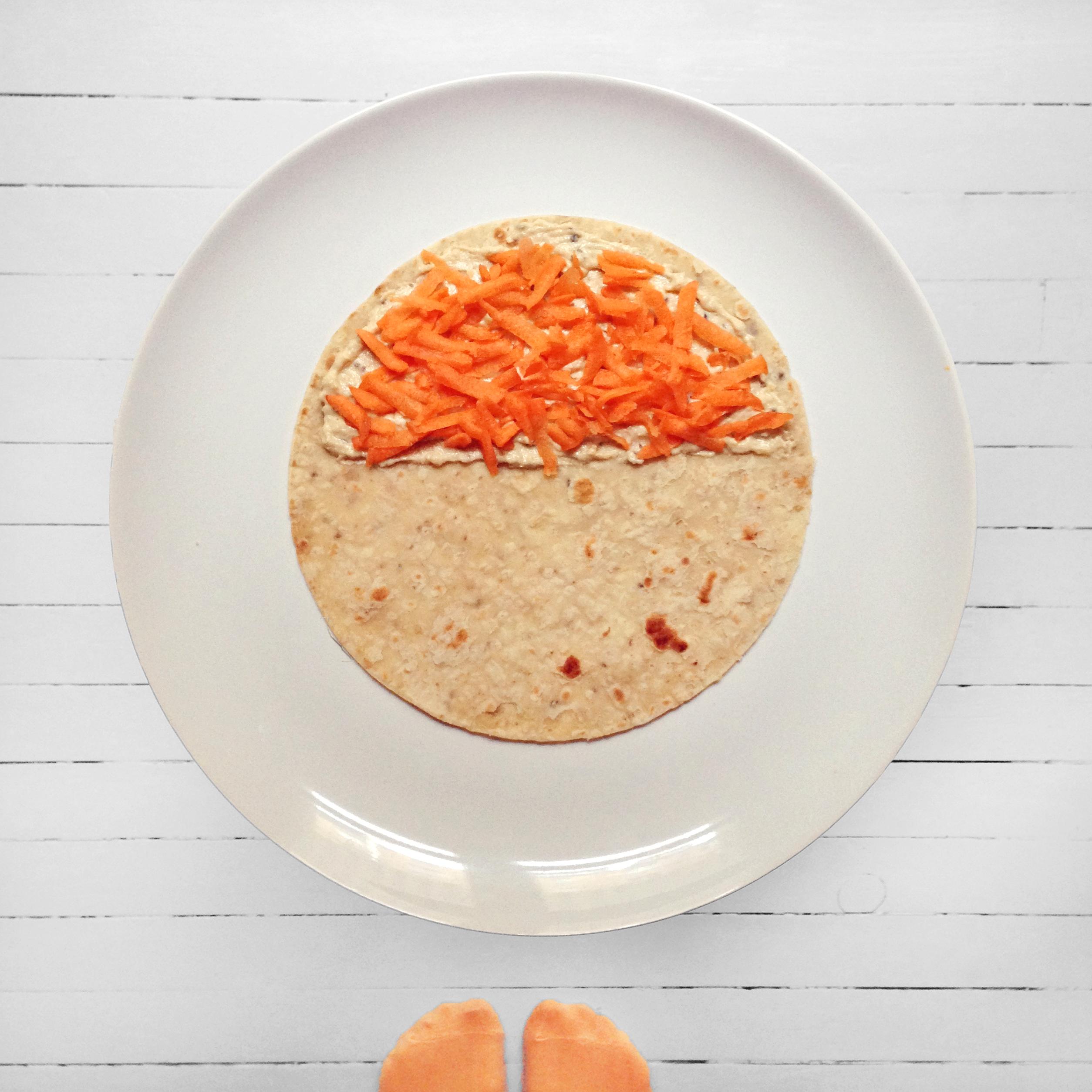 Smør hummus på den ene lompehalvdelen og strø over revet gulrot, brett over. Ha på mandelsmør og revet eple på den andre lompen, brett over på samme måten.