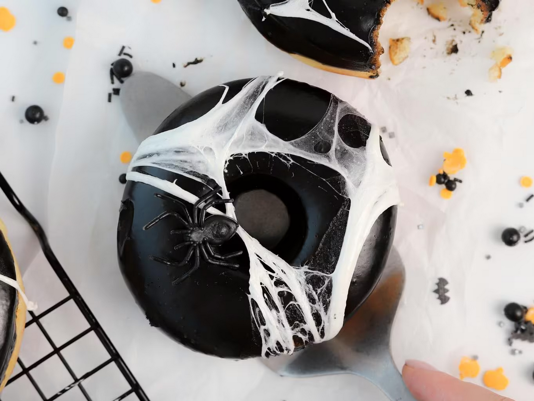 Ta litt marshmellow mellom fingrene og strekk det ut til det ser ut som spindelvev. Legg det over en donut og plukk opp donuten slik at du får festet spindelvevet på undersiden av donuten.  