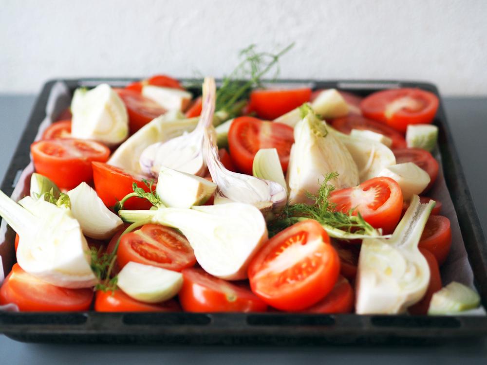 Start med å vaske og dele alle tomatene i to. Legg dem med snittflaten opp på et stekebrett. Vask og del fennikelen i mindre biter og fordel dem utover brettet. Skrell og del løken i mindre biter. Del den ferske hvitløken i to, med skallet på.