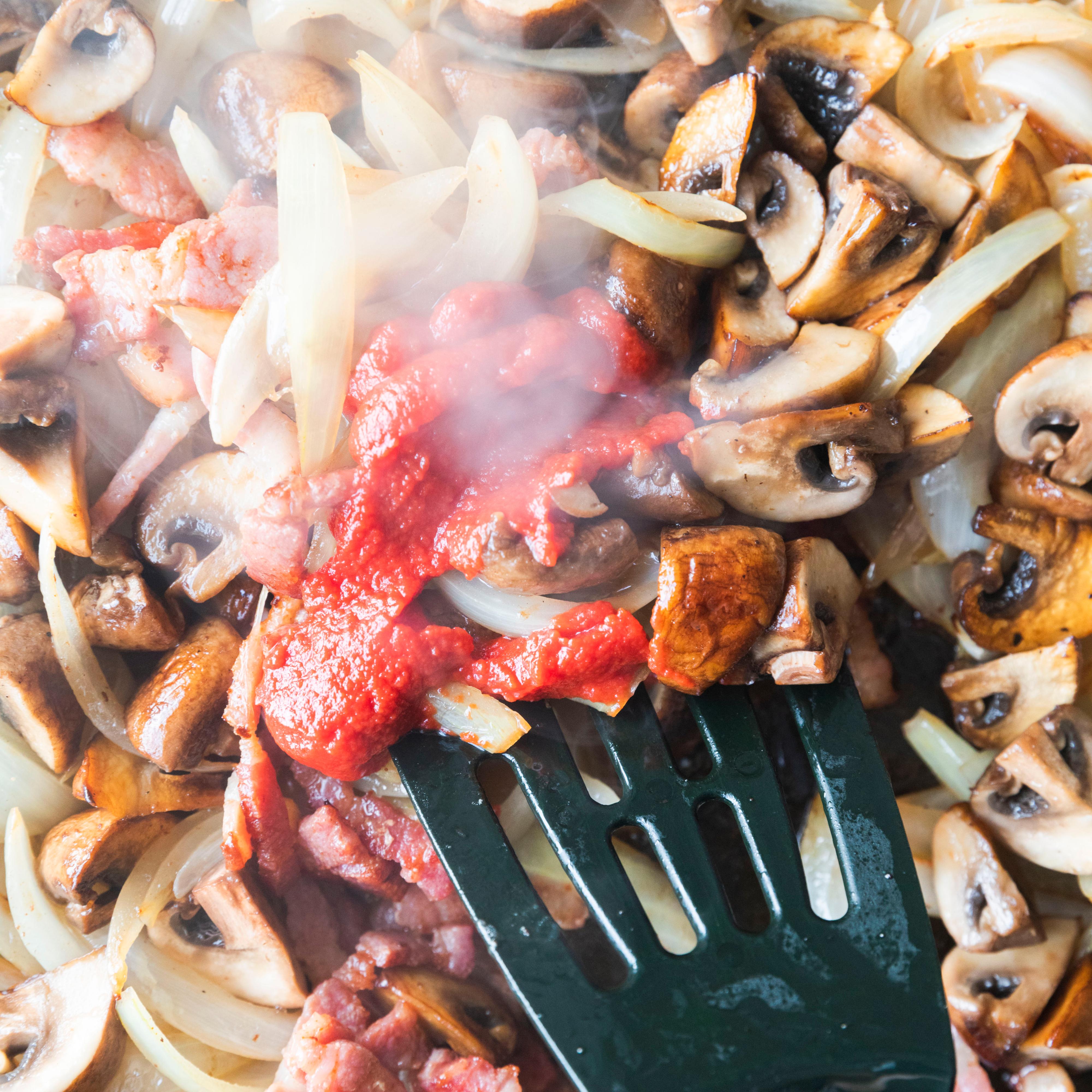 Ha bacon, løk og sopp tilbake i pannen. Rør inn tomatpuré og tilsett kraft og fløte. La det koke til sausen har tyknet.