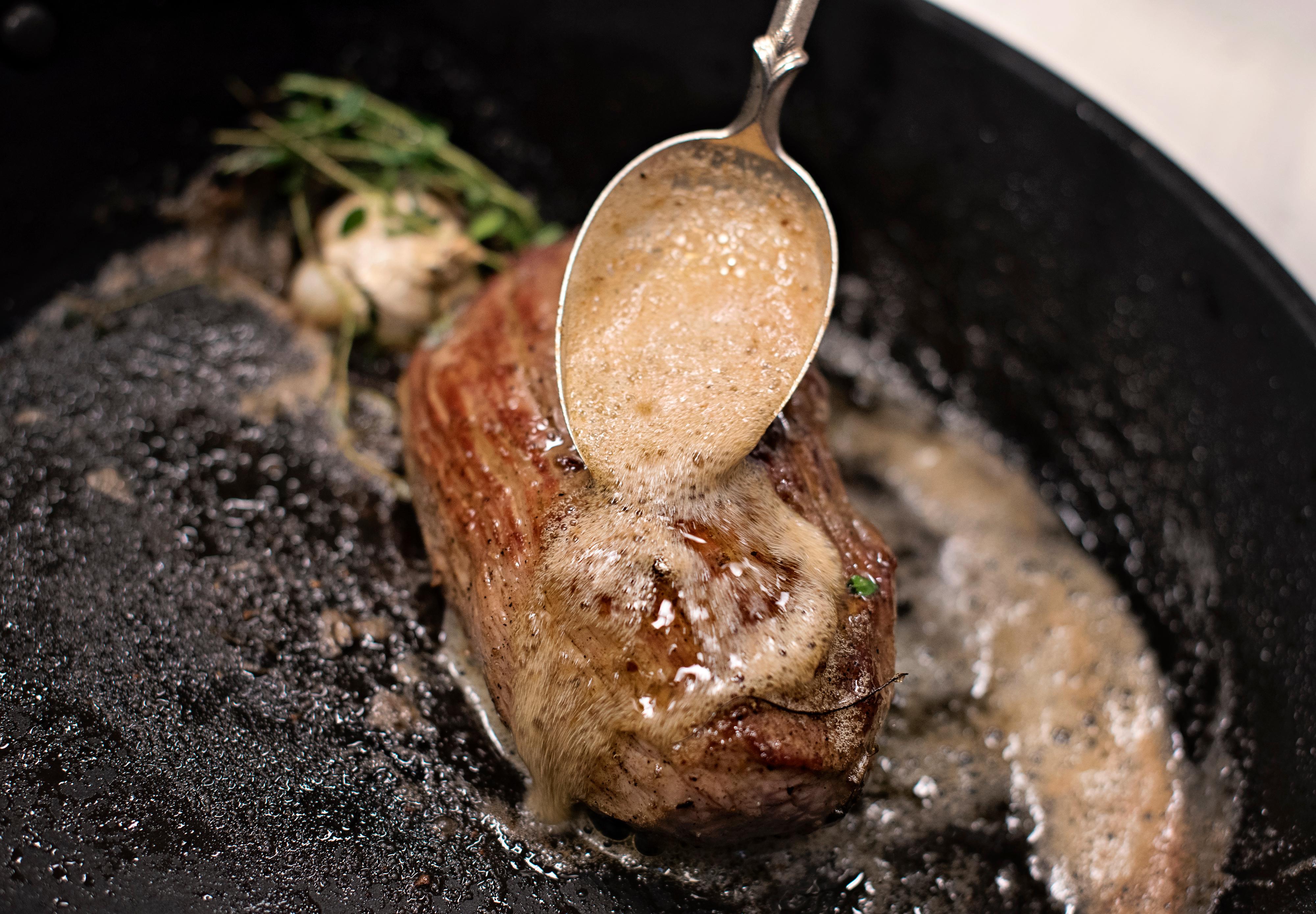 Skru ned temperaturen og tilsett timian, hvitløk og smør. Bruk en skje til å øse smøret over kjøttet for ekstra god smak.
