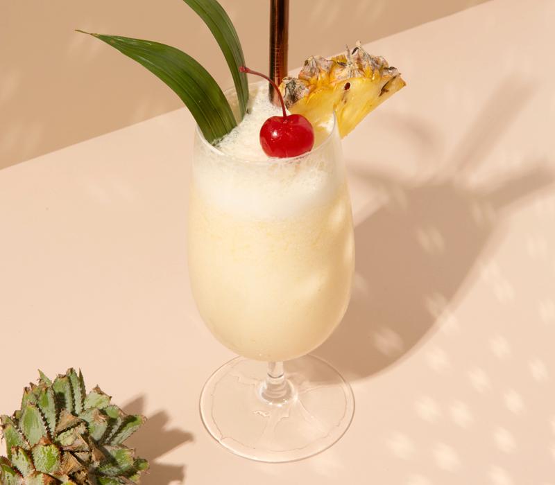 Et glass piña colada pyntet med et cocktailbær og en skive ananas.
