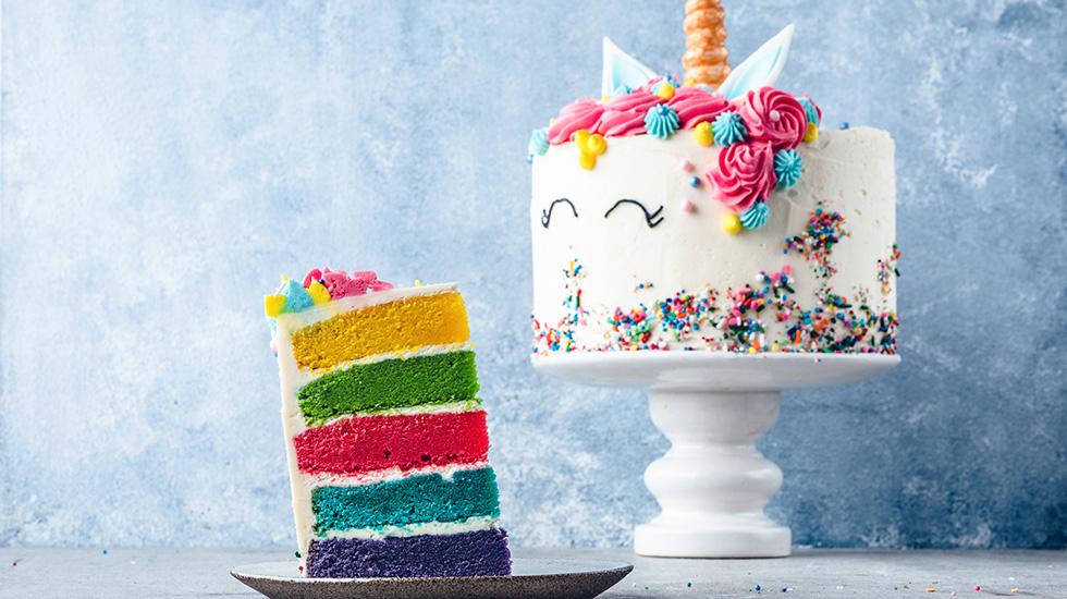 Enhjørningkake på kakefat med stett, og en kakebit med regnbuefarger