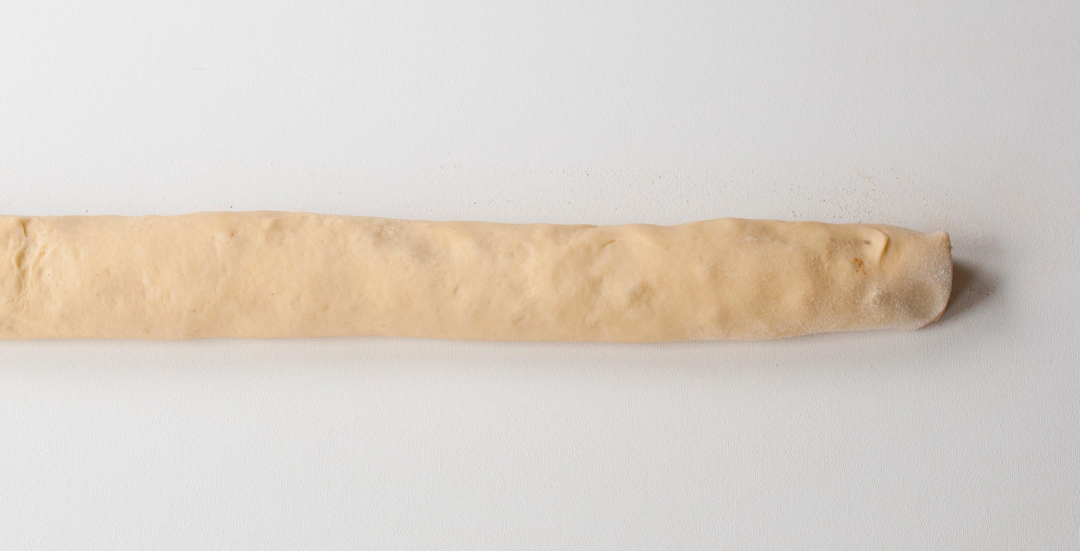Når deigen er hevet kjevles den ut til et rektangel som er omtrent 80 cm bredt. Smør smøret jevnt utover leiven og dryss over sukker, kanel og mandler. Rull leiven sammen fra langsiden, på samme måte som når du lager kanelsnurrer. Legg rullen med skjøten ned.
