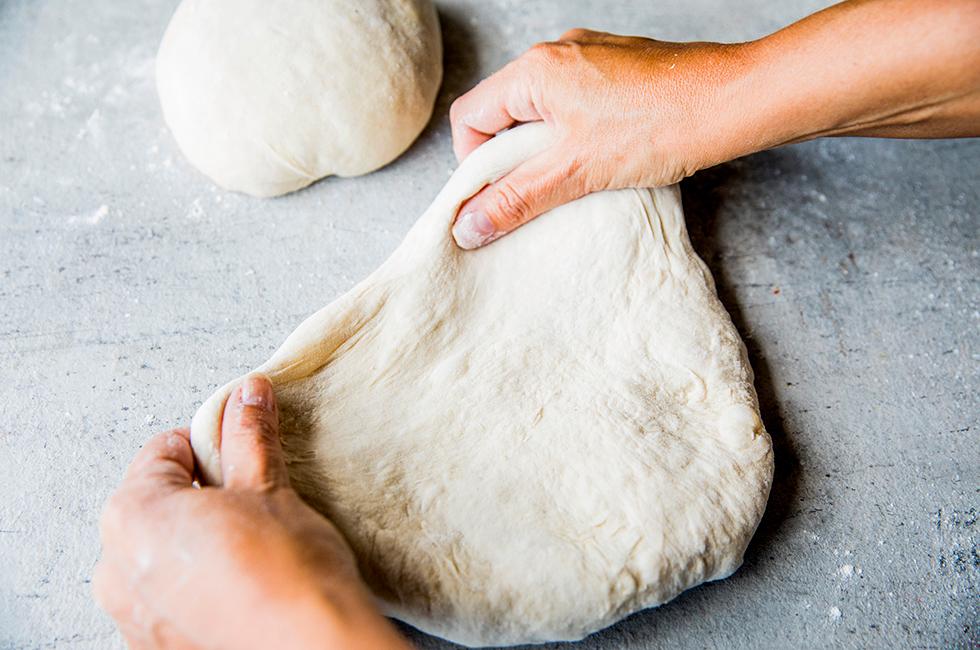 Varm ovnen til 225 grader. «Dra» deigbollene ut til to fine pizzabunner og legg dem over på hvert sitt stekebrett med bakepapir.
