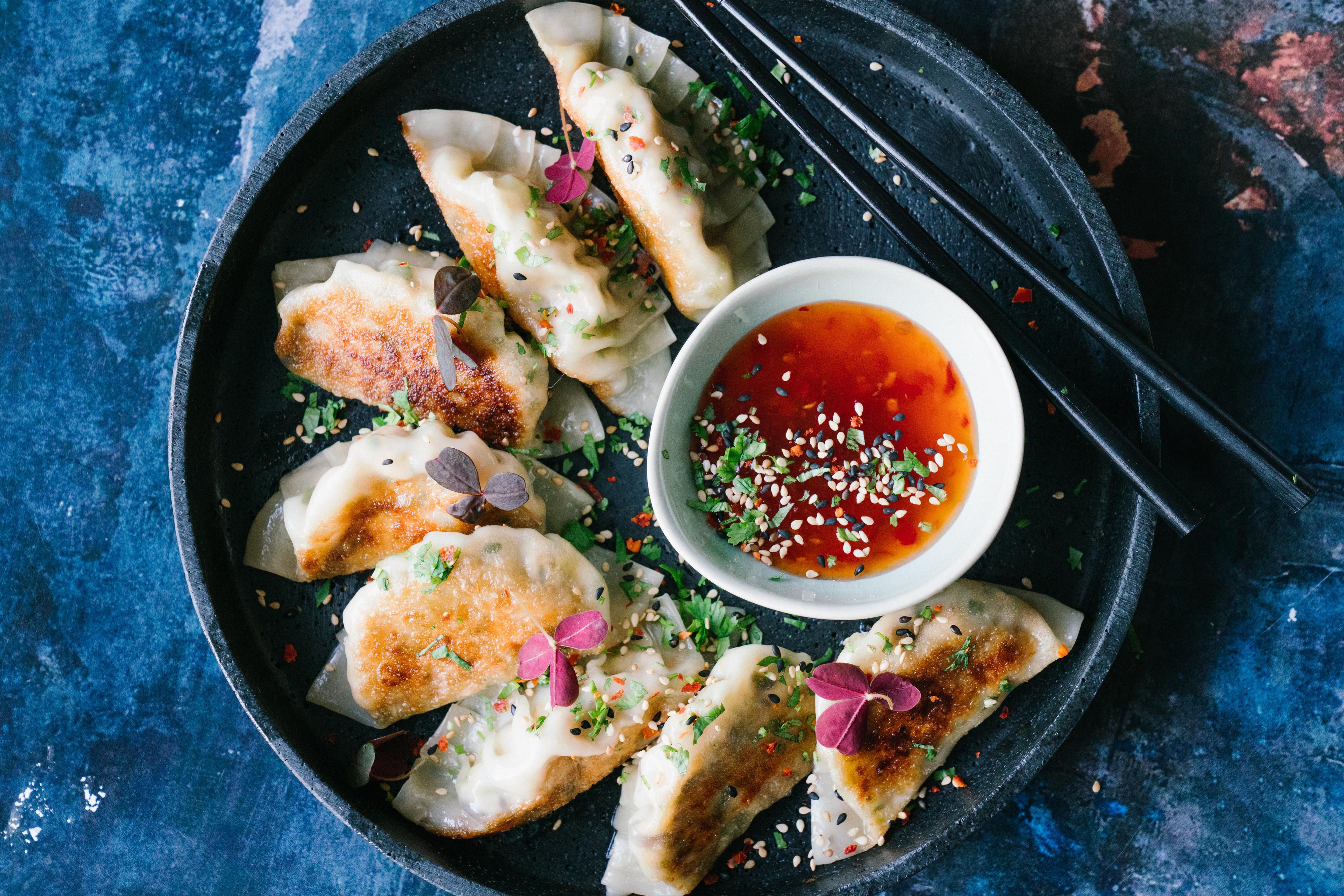 Åtte potsticker dumplings og en skål med søt chilisaus servert på et rundt svart fat med kant.