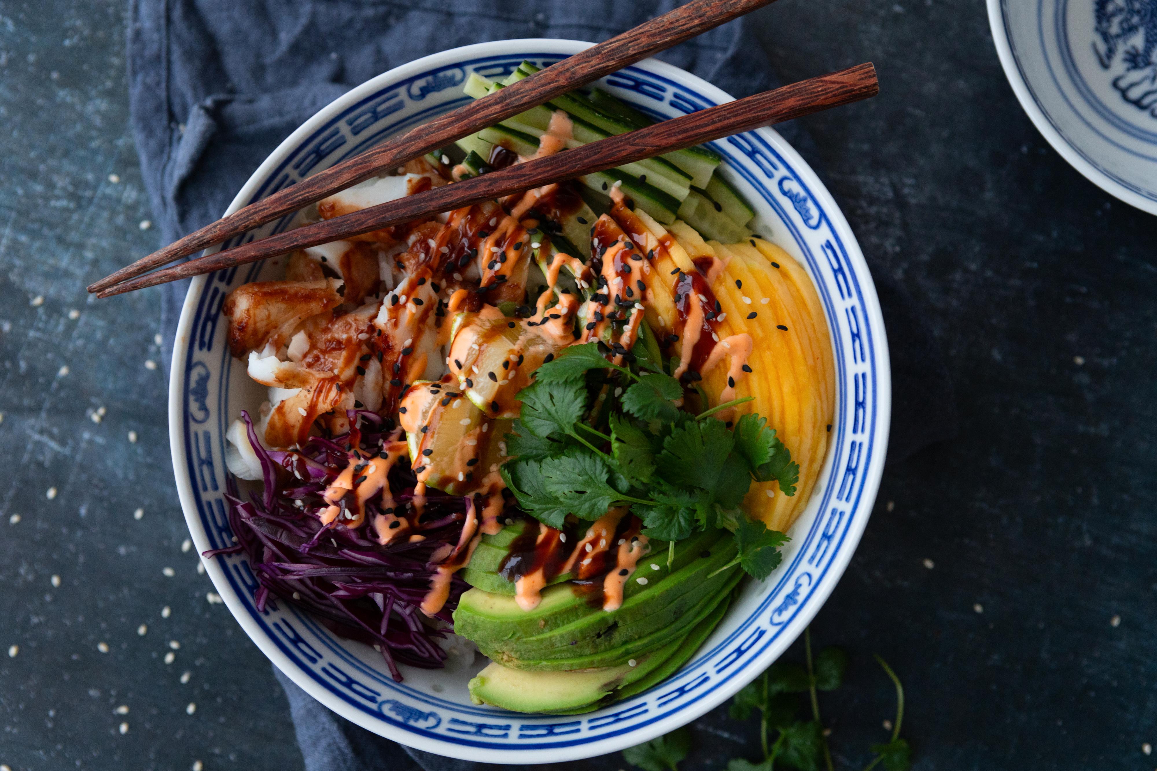 En bowl med sei, mango, avokado, ris og hoisinsaus, dekorert med spisepinner