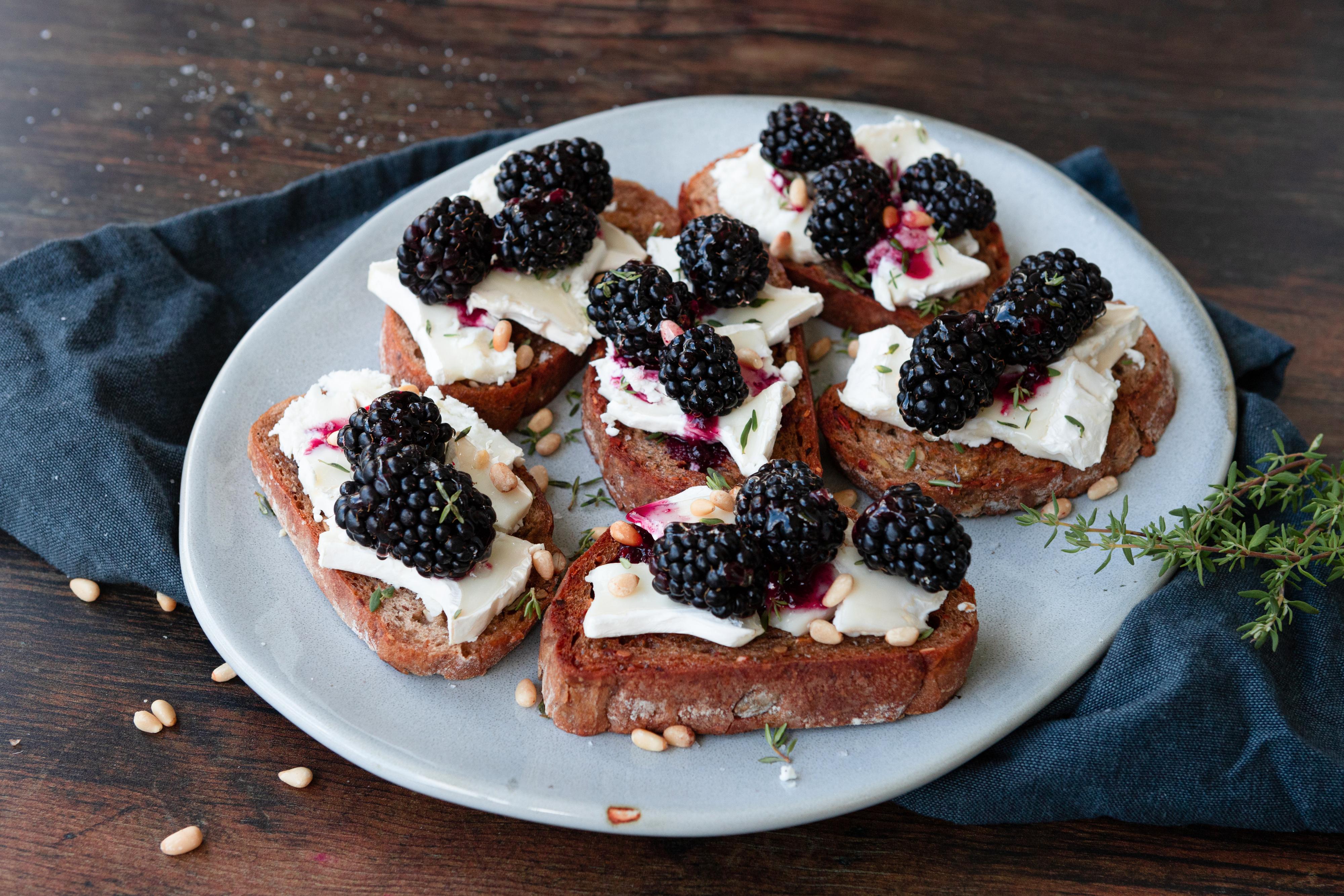 Et fat med mange små skiver bruschetta toppet med chèvre og bjørnebær