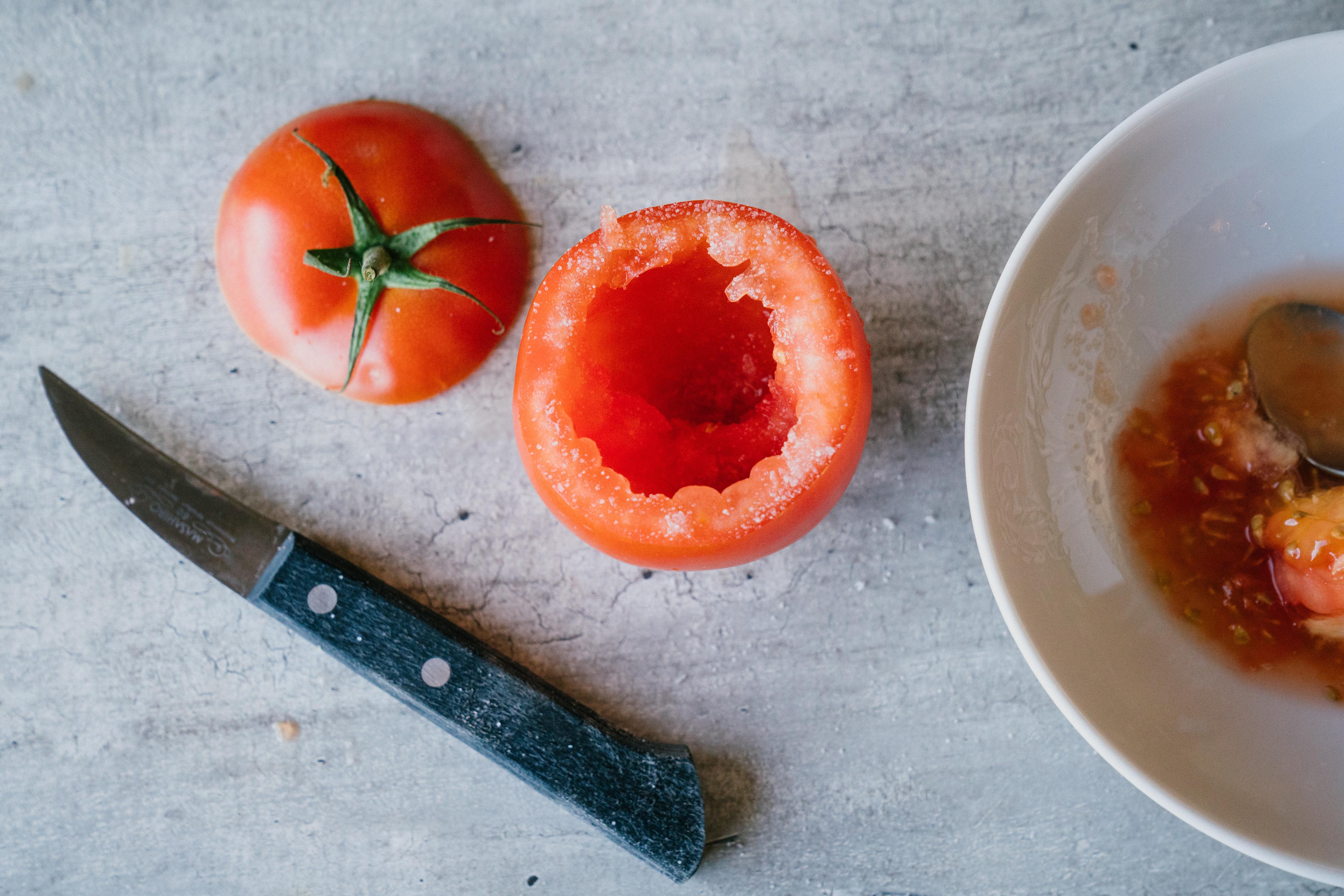 Skjær av toppen på tomatene. Bruk en spiss liten kniv og fjern det harde stilkfestet i tomatene. Skrap ut innholdet i tomaten med en liten skje, og gni alt gjennom en sikt. Ta vare på all tomatsaften, fjern det meste av frøene og hakk opp bitene av tomatkjøtt. Dryss litt salt over tomatene og la de stå på en liten rist - eller i en liten form med kjøkkenpapir - med kjøttsiden ned. 