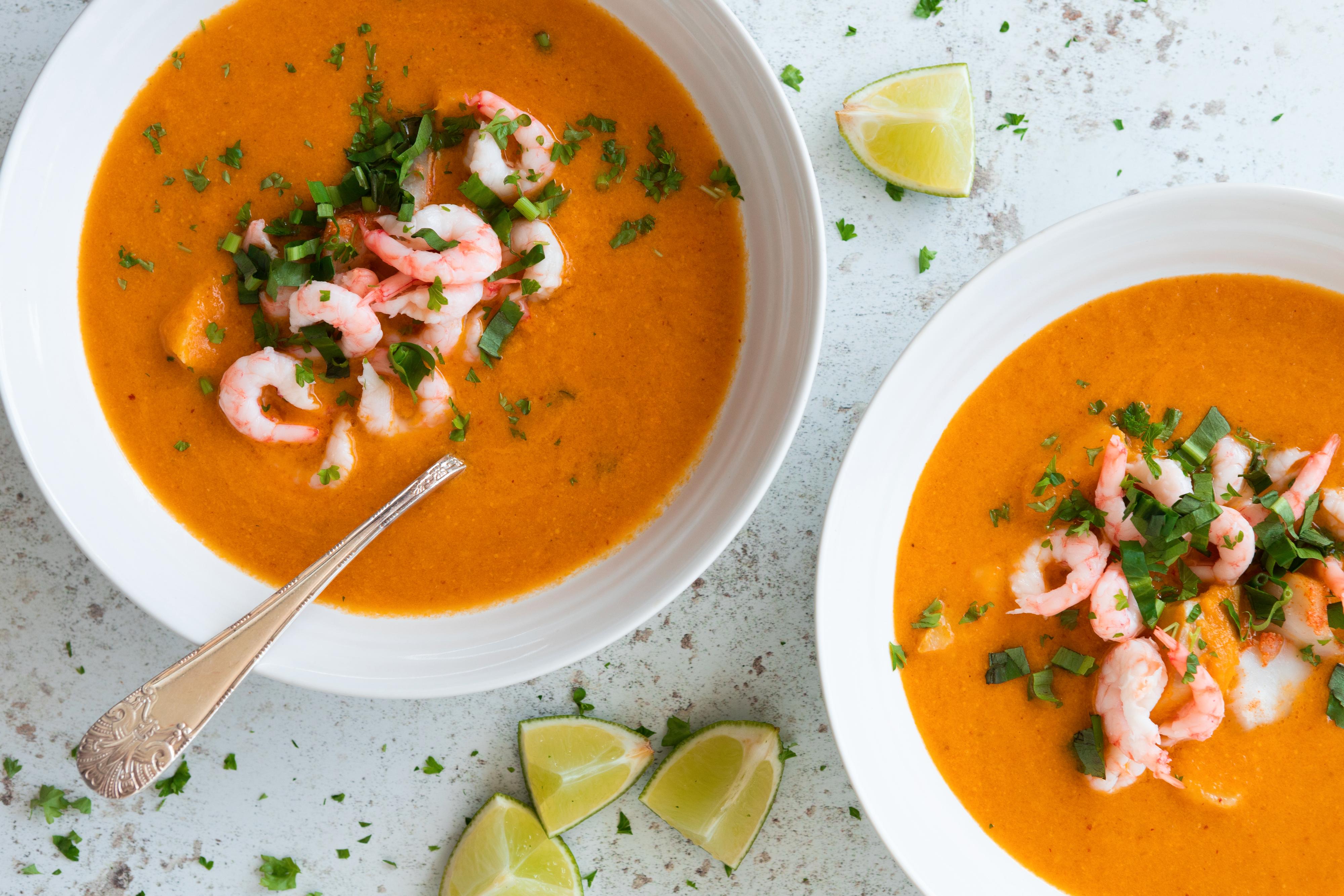 To skåler med rød fiskesuppe, toppet med reker og urter