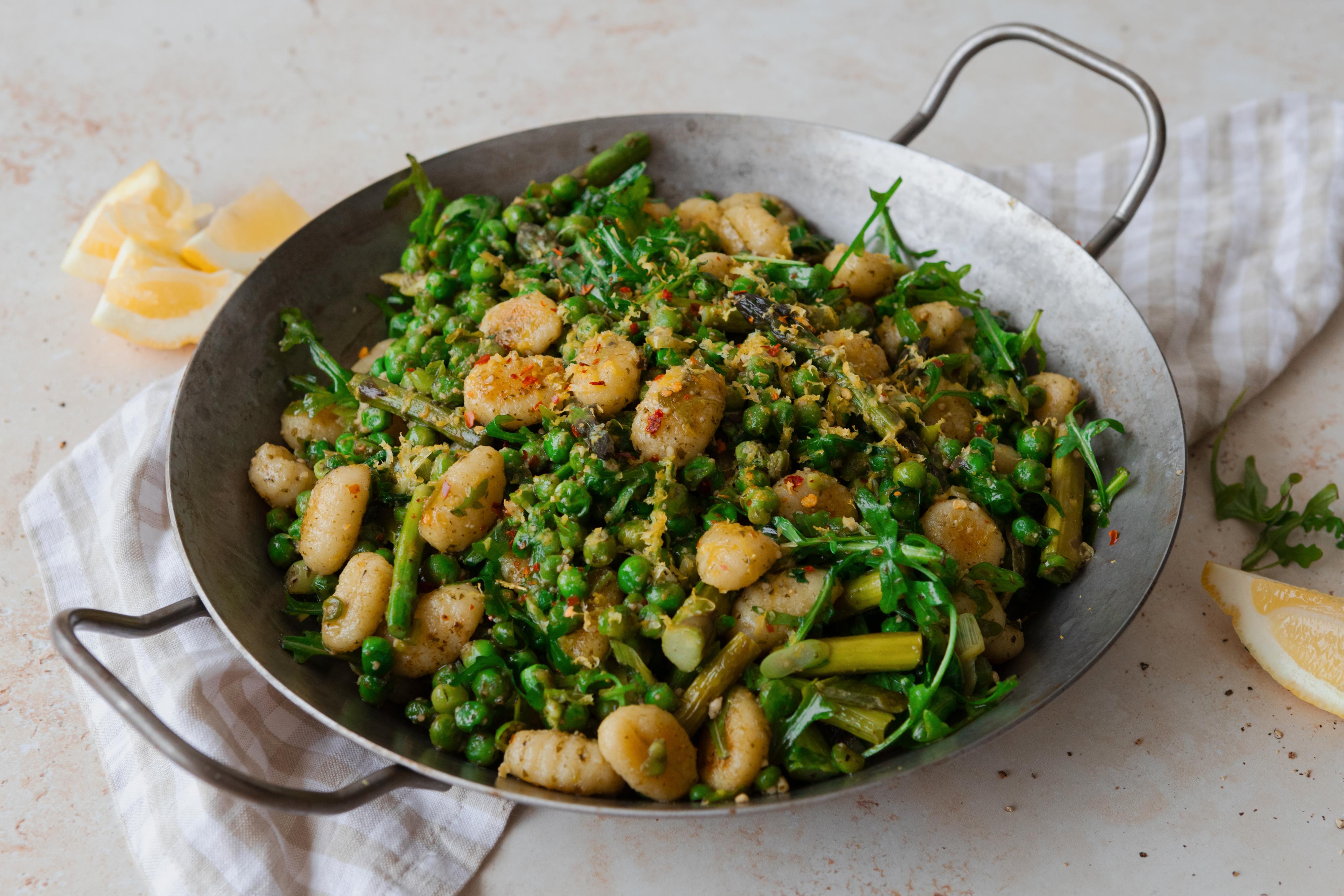 I en wokpanne med håndtak ligger en rett med gnocchi iblandet pesto og grønne grønnsaker.