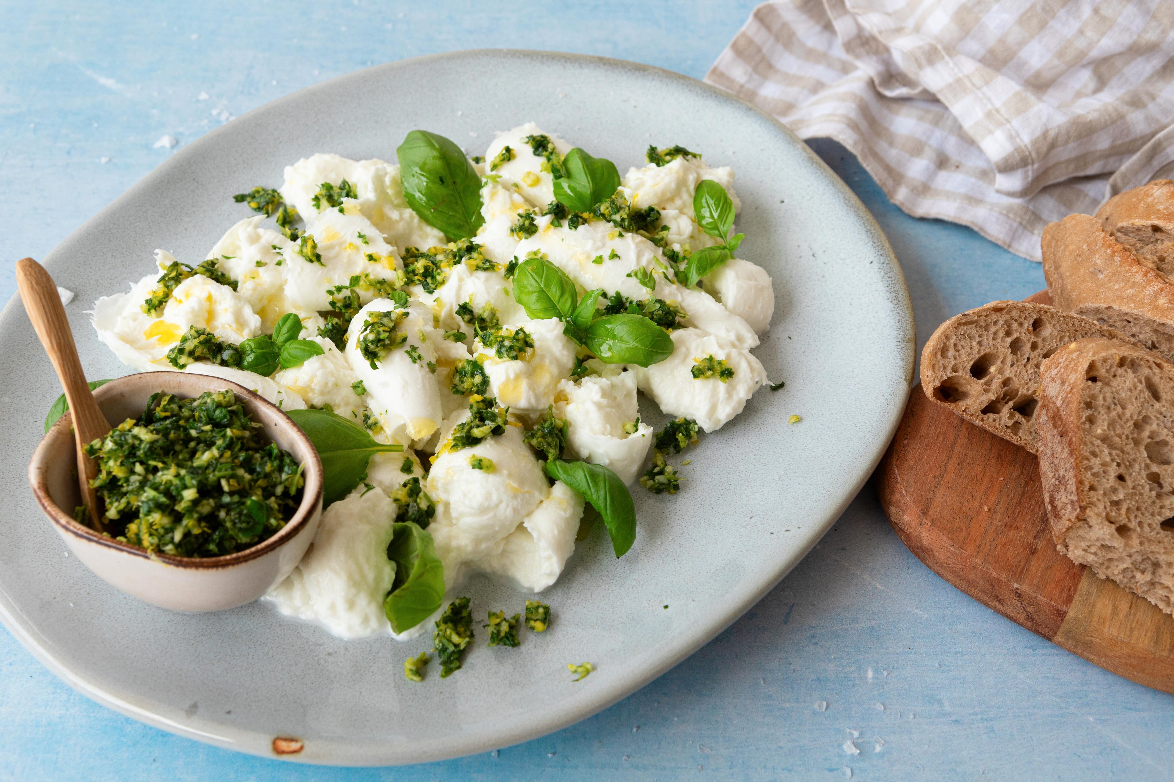 På en tallerken ligger en skål med gremolata og opprevet mozzarella, toppet med gremolata.