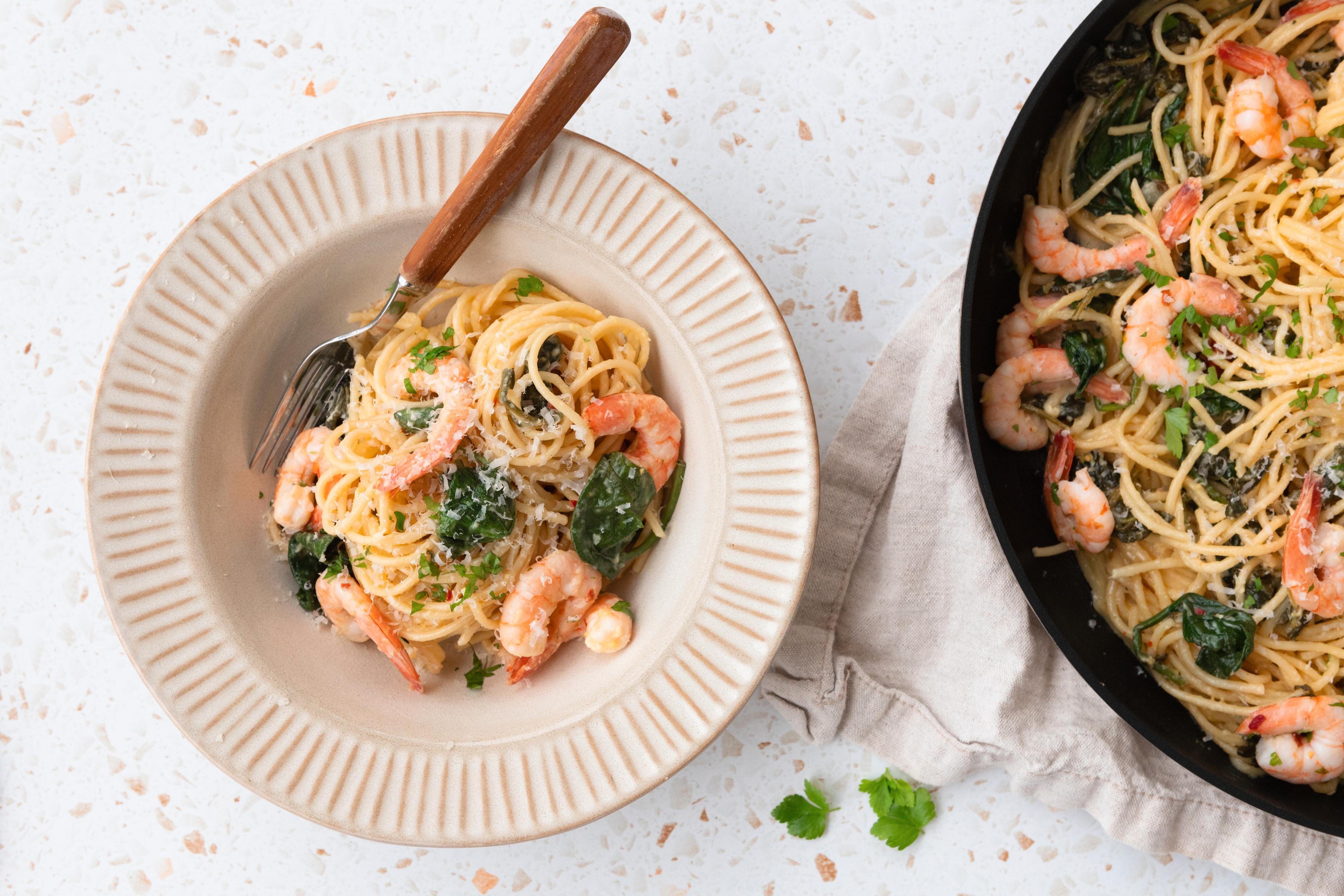 I en dyp beige tallerken ligger pasta med scampi, spinat og et dryss parmesan.